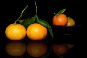 Group of four whole fresh orange mandarin in glazed bowl isolated on black glass