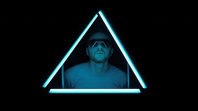 Young man puts on sunglasses and bobs head rhythmically while looking through flickering colored triangle of light.