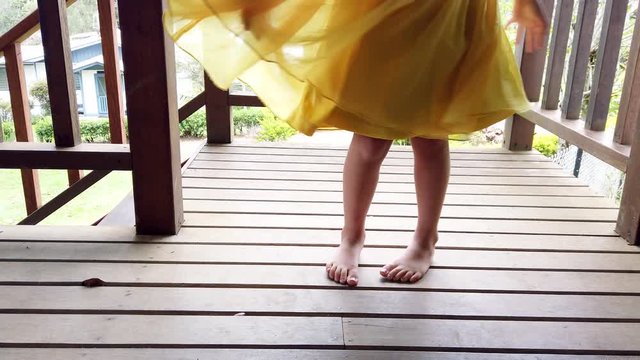 Carefree and playful little girl twirling in yellow dress on verandah