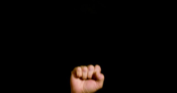 Raised fist gesture for support or solidarity, often socialist, male hand isolated on neutral black background, 4k video studio shoot
