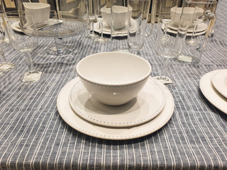 White porcelain in the foreground and glasses in the background on a linen tablecloth for sale