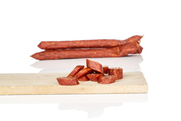 Lot of whole lot of slices of piquant smoked sausage on wooden cutting board isolated on white background