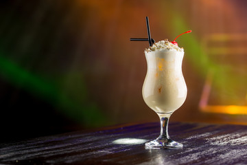 Pina Colada cocktail with whipped cream and cherry on the table in nightclub background