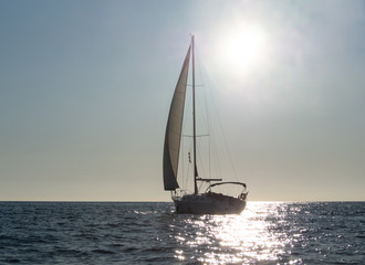 Fototapeta premium Silhouette of sailing yacht on glowing sea water at sunset background