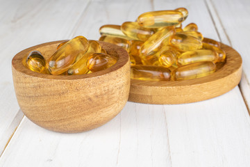 Lot of whole golden fish oil on round bamboo coaster in bamboo bowl on white wood