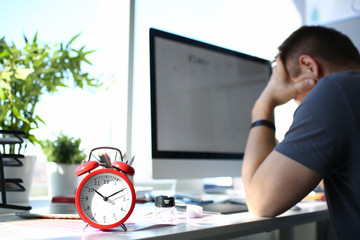 Red alarm clock stand at worktable with thoughtful man in background closeup