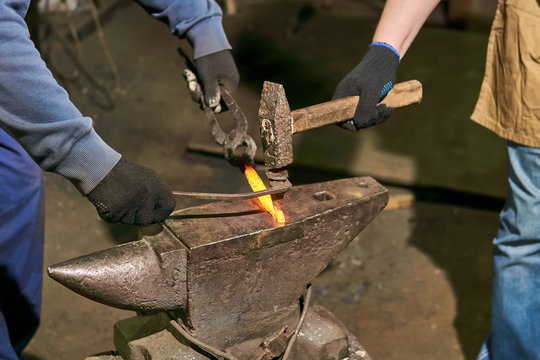 blacksmith with striker forges a horseshoe, close-up
