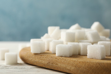 Board with sugar cubes on wooden background, close up