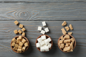 Bowls with different sugar on wooden background, top view