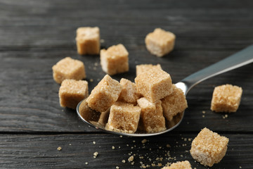 Spoon with sugar cubes on wooden background, close up