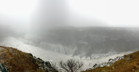 Breathtaking scenery at the Gullfoss Golden Waterfall landmark, a nature attraction in Iceland: Arctic nature with majestic rocks, the Hvita river running in the winter canyon with a cloudy white sky