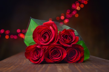 Beautiful Red Roses Piled in Bouquet Wrapped in Green Paper with Red Bokeh Lights