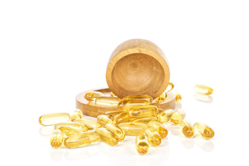 Lot of whole golden fish oil capsules on round bamboo coaster in bamboo bowl isolated on white background