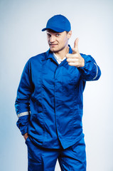 Portrait of young worker man wearing blue uniform. Pointing finger at you looking at camera....
