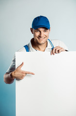 Mockup image of a young smiling worker holding empty white banner and points to it.