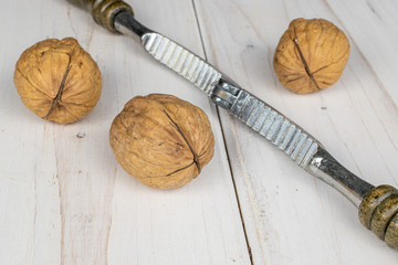 Group of three whole tasty brown walnut with wooden nutcracker on white wood