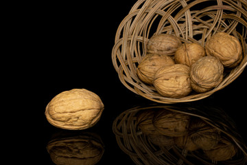 Group of seven whole tasty brown walnut in round rattan bowl isolated on black glass