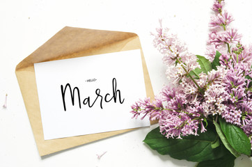 Inscription Hello March. Lilac flowers and envelope on white background. Spring flowers. Top view, flat lay. - Image