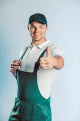 Portrait of young worker man wearing green uniform. Showing thumb up. Movement cool. Isolated on grey background with copy space. Human face expression, emotion. Business concept.