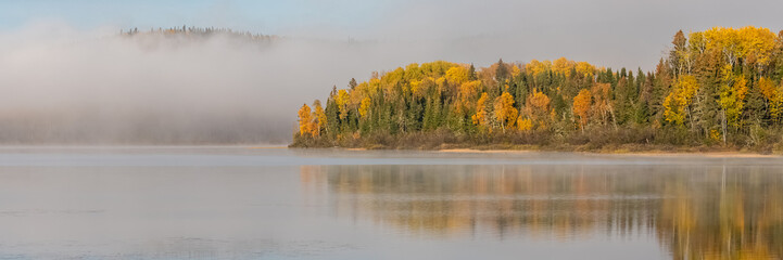 A lake in the forest in Canada, during the Indian summer, with fog on the water in the morning