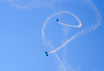 Naklejka na ściany i meble Two parachutists perform at an air show, leaving white smoke traces in the blue sky.