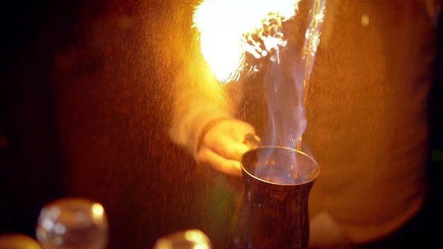 Cooking punch or grog. Adding cinnamon gives a bright flash of fire. It can be a Blue Blazer or grog.  Dark scene, close-up. 
