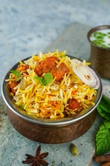 Homemade Chicken tikka Biryani served in a traditional brass vessel with yogurt dip, selective focus