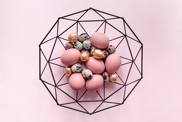 on a pink background there is a beautiful forged basket with gold colored Easter eggs copy space...