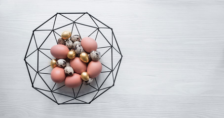 on a light wooden background there is a beautiful forged basket with gold colored Easter eggs copy...