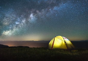tourist tent of yellow color against the night sky with the Milky Way