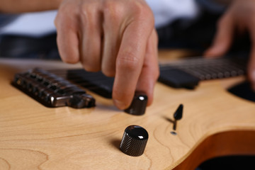 Male arms holding and playing classic shape wooden electric guitar closeup. Six stringed learning...