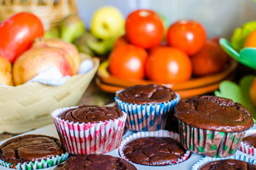 Photograph of homemade chocolate and vegan muffins with fruit and vegetables in the background in the home kitchen