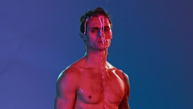 Vivid neon style photo session of young handsome gay man or freak stripper. Red and blue light on athletic built guy, isolated background, thick white liquid flowing over head and tattooed body