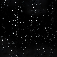 Falling Rain water drops on a black dramatic window glass. Autumn  depression background. Rain pattern.