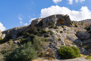 Beautiful view of big mountain with grotto Aeolian Harp on trail Alchak-Kaya. Alchak Cape in south coast of resort Sudak city, Crimea, Russia.