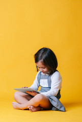 Fototapeta premium A caucasian girl in a gray dress and white shirt uses and plays with a tablet on a yellow background