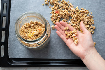 Granola on female hand and glass jar on parchment paper on baking sheet, top view. Made homemade healthy breakfast