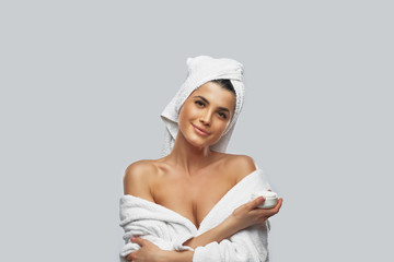 Woman in bathrobe holding cream jar.