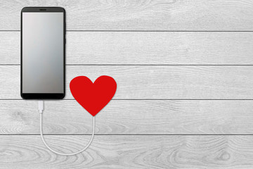 concept of the power of love, on white wooden background  isolated Mobile smart phone with blank screen that is charging from red heart