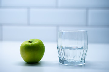 An apple and a glass of mineral water. Healthy breakfast. Modern white kitchen.