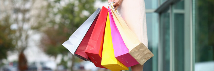 Focus on beautiful stylish female in stylish clothes and in high heel shoes holding multicolored packages. Fashion and shopping concept. Blurred background