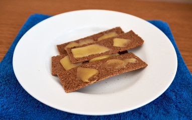Dietary simple toasts dark bread crisps topped with melted cheese on a white round plate on a blue towel on a wooden table. home cooking