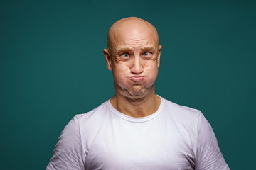 portrait of a bald man puffed out his cheeks on a blue background - obrazy, fototapety, plakaty
