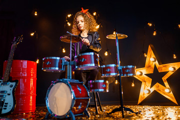 Beautiful girl with curly hair playing the drums on a black illuminated background