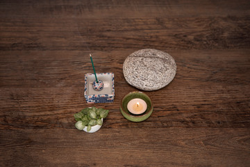 Wellness deco arrangement with burning candle, incense sticks, round stone and fresh leaves on wooden table,  view from above. Mindfulness, meditation concept. Zen style background. 