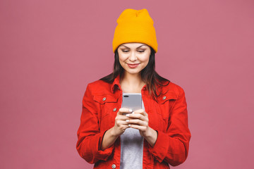 Photo of cheerful cute beautiful young woman chatting by mobile phone isolated over pink wall background.