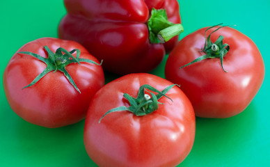 Bright red tomatoes and bell pepper on a green background
