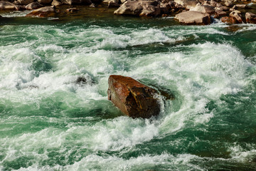 a large stone lies in the middle of a mountain river, the river flows and goes around the stones. Creation of river foam