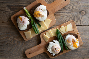 Breakfast for two: poached eggs on rye bread with cheese and green onion served on cutting boards