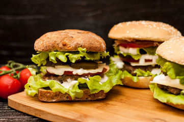 American burgers on a wooden Board with tomatoes on a dark background